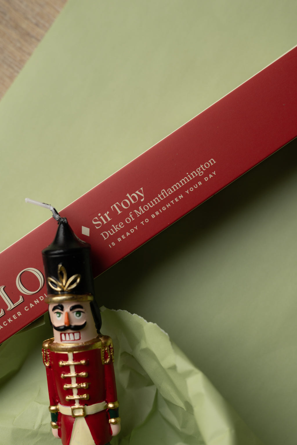 Noello Sir Toby – Detail der Nussknacker-Kerze mit roter Geschenkbox auf grünem Papier; Herstelleraufnahme